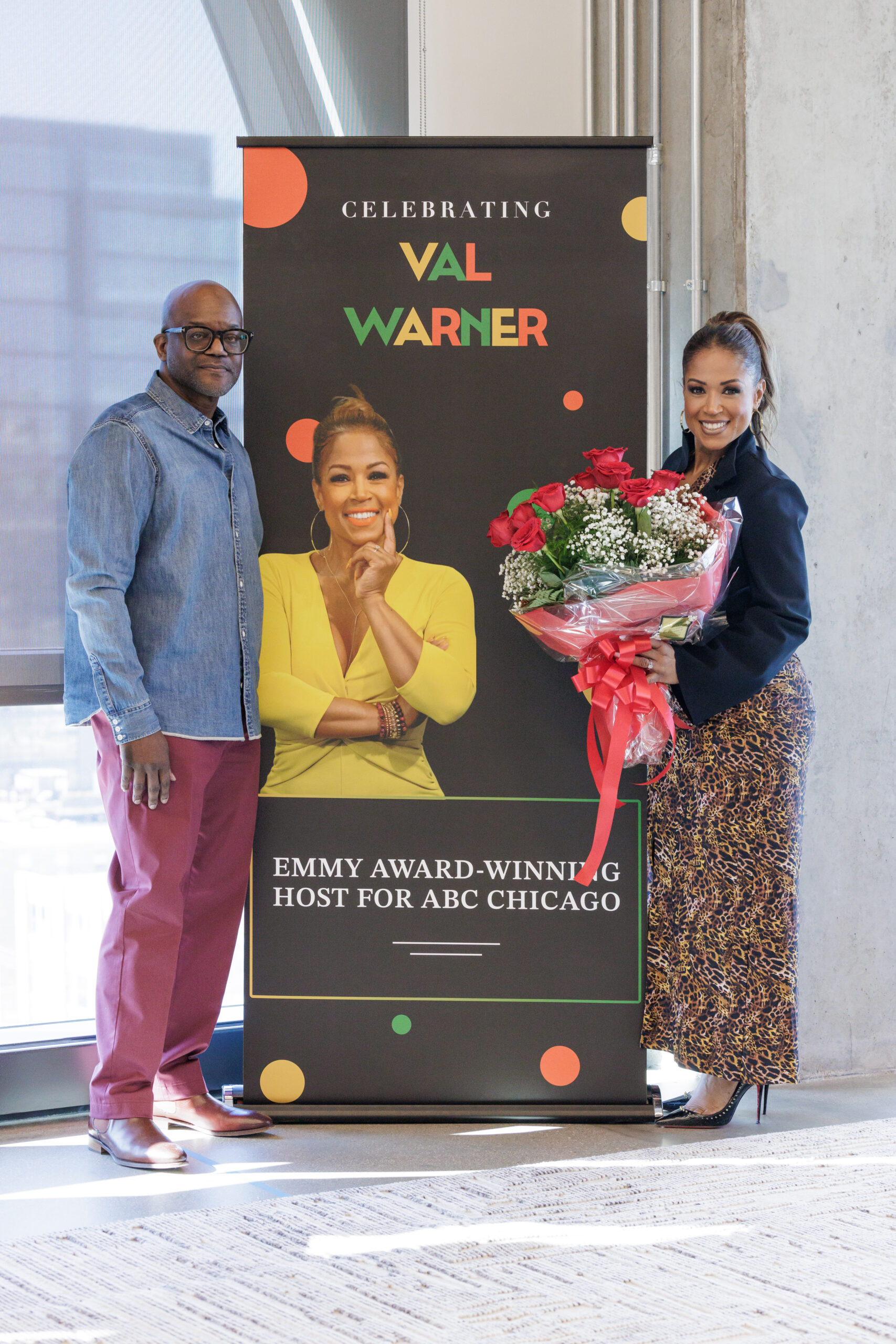 Val Warner pose avec son poster de la série de conférences BOLD et des fleurs à côté de Chip Joseph.