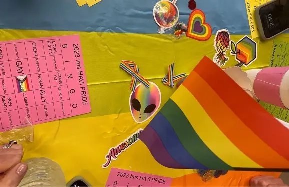 A pride bingo board on a rainbow tablecloth with pride flags
